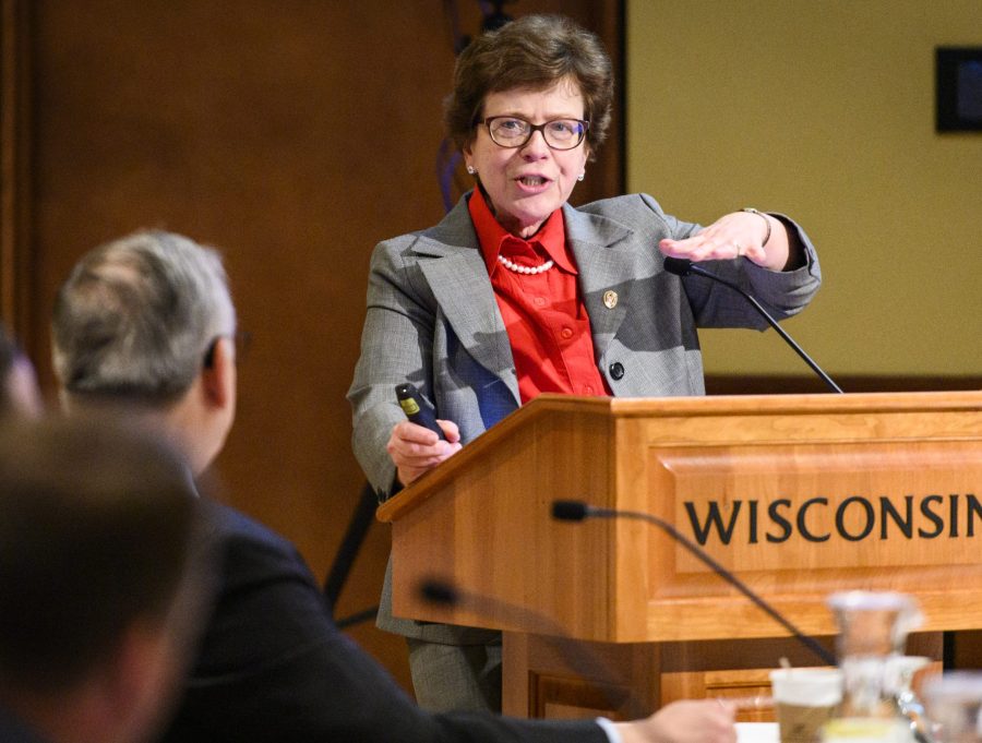 Standing at a lectern, Rebecca Blank raises her left hand to gesture as she addresses a seated audience.