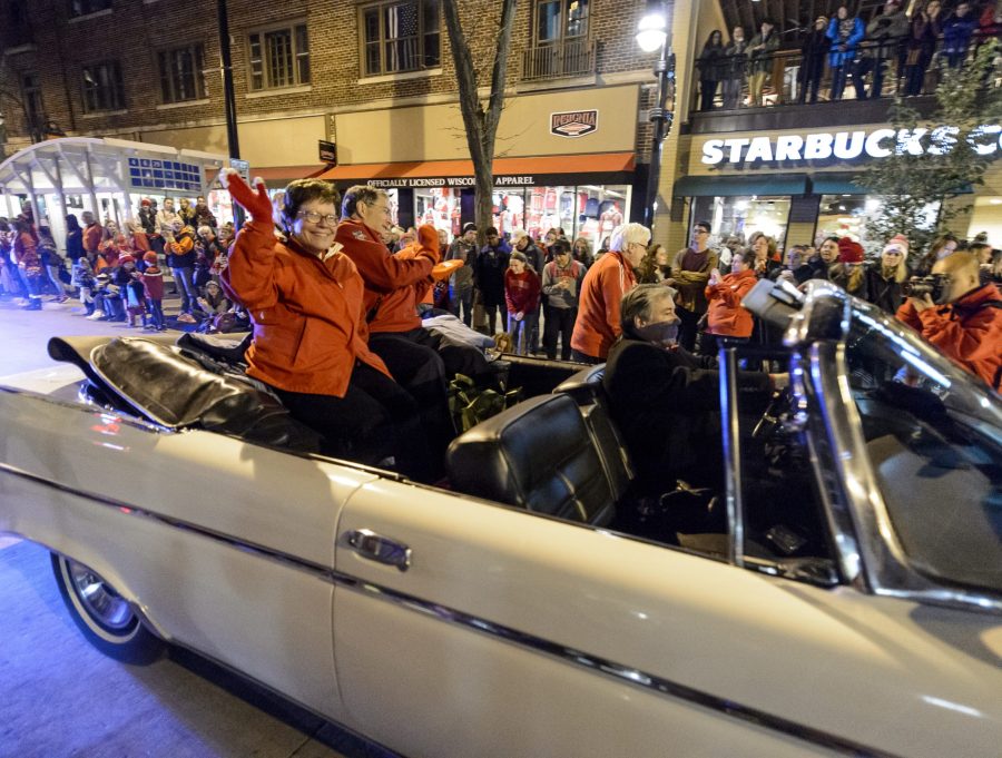 Rebecca Blank and husband Hanns Kuttner sit on the back of an open-top convertible and wave to the crowds of people gathered along State Street for the annual homecoming parade. Blank and Kuttner smile and wave at the onlookers.
