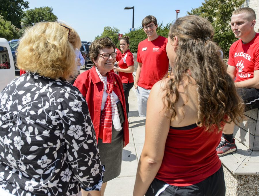 Rebecca Blank stands outside Elizabeth Waters Residence Hall on a sunny day. She is surrounded by a small group of parents and students dressed in red, white and black. It's move-in day at the residence hall.