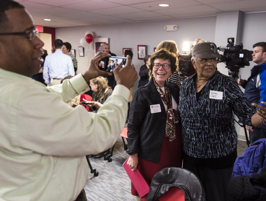 In a crowded conference room, Rebecca Blank stands with her arm around Verline Gee. Gee's son, Rev. Alex Gee takes a photo of the pair.