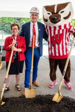 A posed photo at a groundbreaking ceremony showing Chancellor Rebecca Blank, Dean Mark Markel, and Mascot Bucky Badger. The three are standing next to each other holding golden shovels.